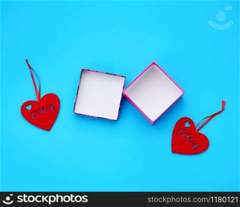 open cardboard square empty box and felt red hearts on a light blue background, top view