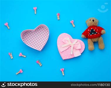 open empty cardboard box in the form of a heart and little brown teddy bear on a light blue background, top view, element for a designer