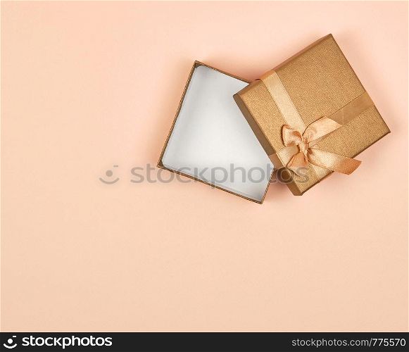 open empty golden square gift box with a bow on a beige background, top view, festive backdrop