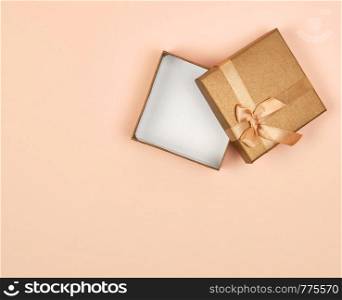 open empty golden square gift box with a bow on a beige background, top view, festive backdrop