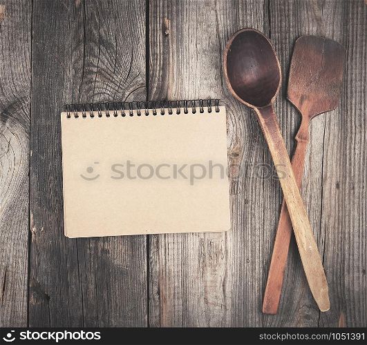 open empty notebook and two wooden spoons on a gray background, top view