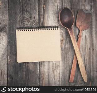 open empty notebook and two wooden spoons on a gray background, top view
