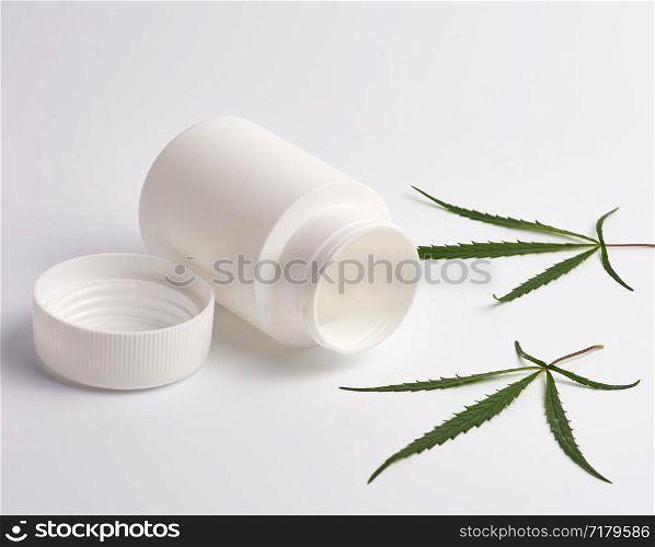 open empty white plastic medical jar for pills and green hemp leaf on a white background, alternative medicine concept