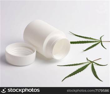 open empty white plastic medical jar for pills and green hemp leaf on a white background, alternative medicine concept
