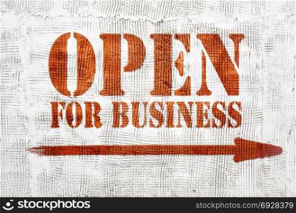 open for business - red graffiti sign with arrow on a white stucco wall
