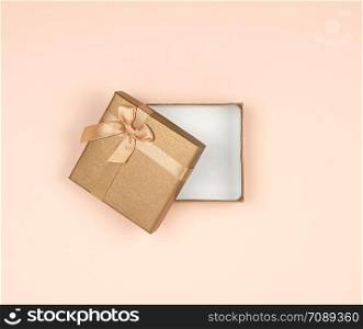 open golden square gift box with a bow on a beige background, top view, festive backdrop