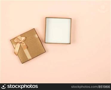 open golden square gift box with a bow on a beige background, top view, festive backdrop