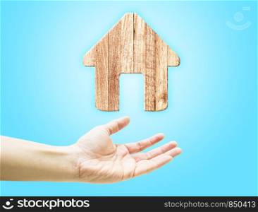 Open hand with wooden plank home icon on light blue background.