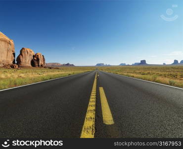 Open highway in scenic desert landscape with distant mountains and butte land formations.