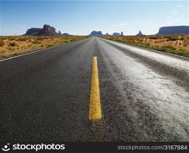 Open highway in scenic desert landscape with distant mountains and mesas.