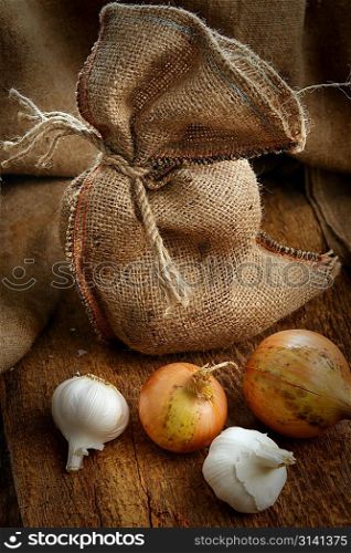 Open jute sack with ripe onions and garlic on wooden board