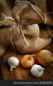 Open jute sack with ripe onions and garlic on wooden board