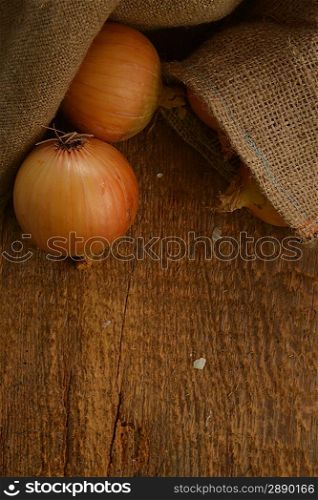 Open jute sack with ripe onions on wooden board