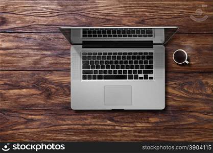 Open laptop and cup of coffee. Open laptop and cup of coffee on brown wooden table. Top view
