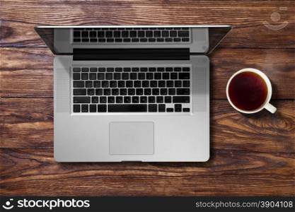 Open laptop and cup of tea. Open laptop and cup of tea on brown wooden table. Top view
