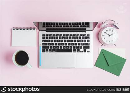 open laptop pencil alarm clock spiral notepad envelope pink background