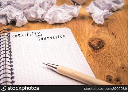 Open math notebook with crumpled drafts in the background, on a wooden desk. The image depicts the effort to obtain creativity and innovation.