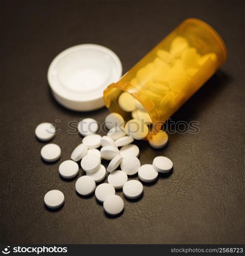Open medicine bottle with pills spilling out onto table.