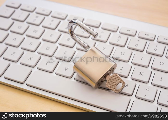 Open metal padlock with key on white keyboard, wooden table on background. Cracking password, encryption, internet access, cyber network, business solution, blockchain transaction concepts.