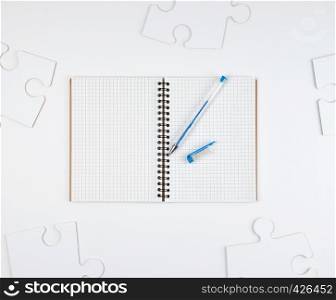 open notebook in a cell and a blue pen on a white background, next to large blank puzzles, top view
