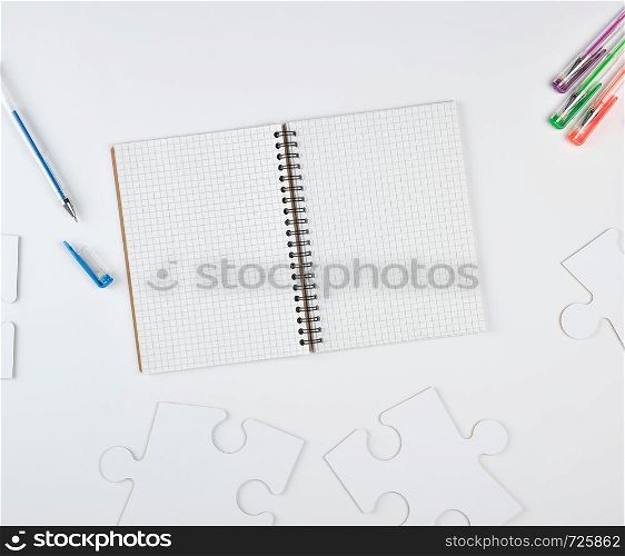 open notebook in a cell and on a white background, next to large blank puzzles, top view