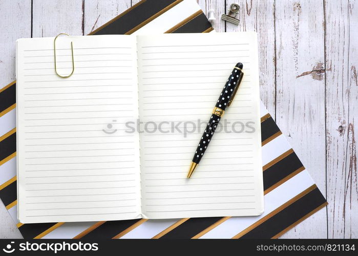 Open notebook in line, a clip and a pen on a wooden background.