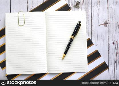 Open notebook in line, a clip and a pen on a wooden background.