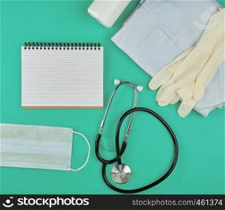 open notebook in line with white sheets, medical mask, stethoscope and bandage on a green background