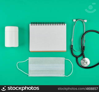 open notebook in line with white sheets, medical mask, stethoscope on a green background