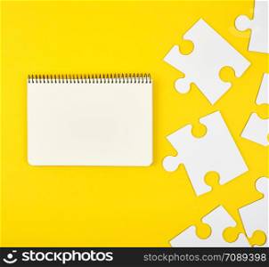 open notebook on a yellow background, next to large white blank puzzles, top view