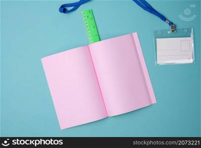 open notebook with blank pink sheets, ruler on blue background, top view