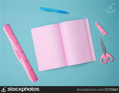 open notebook with blank pink sheets, scissors and ruler on blue background, top view