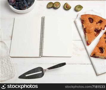 open notebook with blank white pages, baked pie with plums and fresh fruits, top view, flat lay