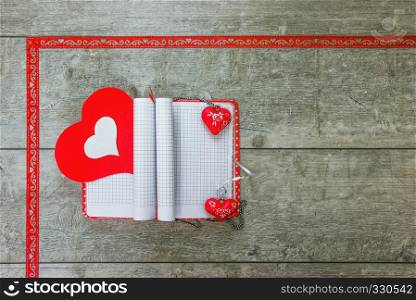 Open notebook with bookmarks and pendants in the form of red and white hearts lying on a wooden table. Gift notebook with red and white hearts