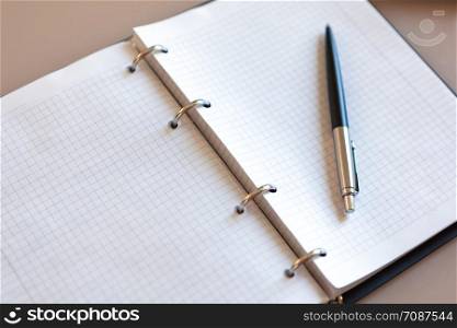 Open notebook with pen lying on it on beige desktop. Notepad sheets on silver brackets, automatic ballpoint pen in silver-black colour. Concept business, work at home. Copy space. Top view, close-up