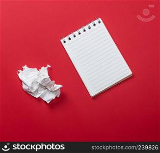 open notebook with white sheets and a crumpled ripped out sheet of paper on a red background