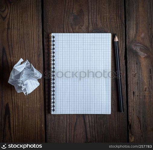 open notebook with white sheets and a crumpled ripped out sheet of paper on a brown wooden background