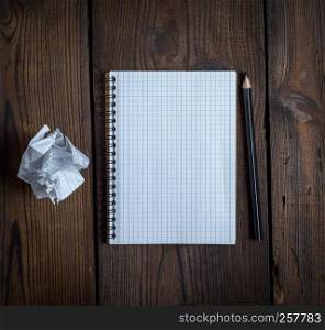 open notebook with white sheets and a crumpled ripped out sheet of paper on a brown wooden background