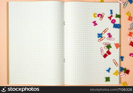 open notebook with white sheets in a cage and small multi-colored wooden letters, back to school, copy space