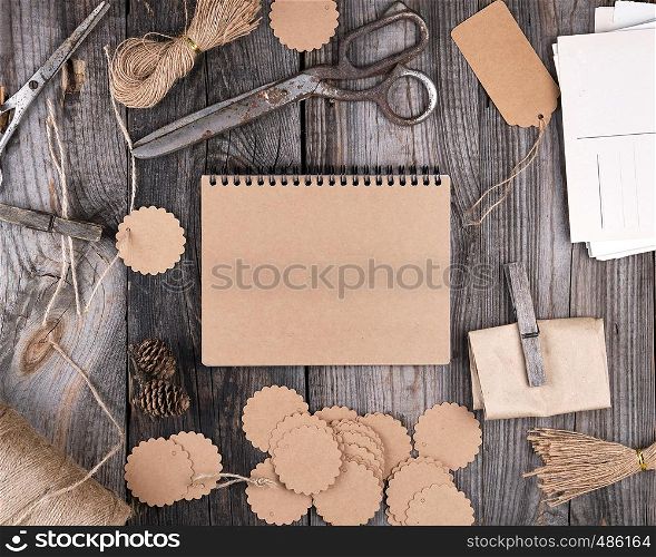 open notepad with brown empty sheets on a gray wooden table, next to it are a rope, paper tags and scissors, top view
