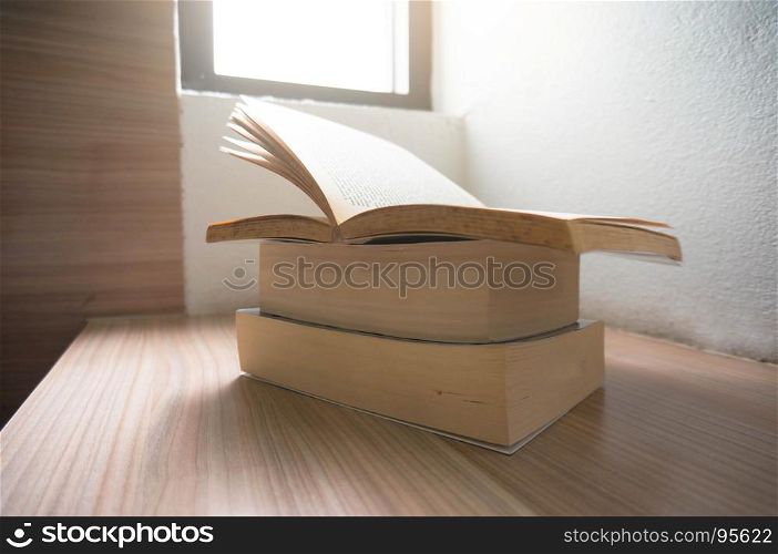 Open old books on a wooden table with window light.