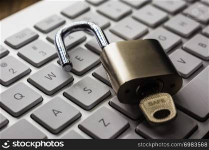 Open padlock with word SAFE on key on white pearl keyboard, dark tone with natural light reflect on objects. Cracking password, encryption, internet access, cyber network, data security concepts.