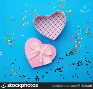 open pink heart-shaped cardboard box on a blue background with multi-colored shiny confetti, festive backdrop for birthday, Valentine&rsquo;s day