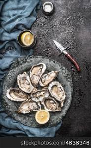 Open raw oysters on vintage plate with lemon and oysters knife, dark rustic background with water drops , top view