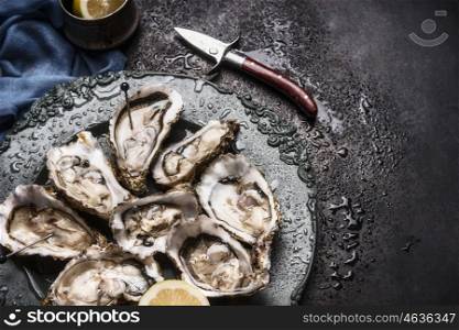 Open raw oysters on vintage plate with lemon and oysters knife, dark background, top view, close up