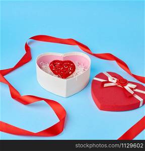 open red heart-shaped gift box with a bow on a blue background, festive backdrop. Valentine gift