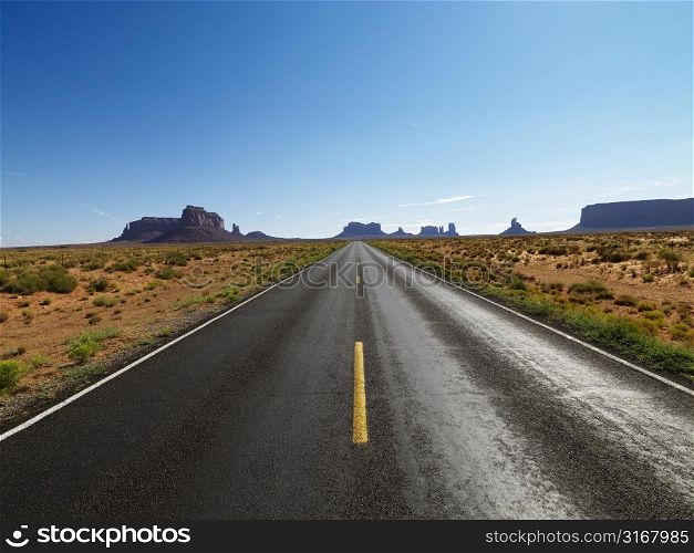 Open road in scenic desert landscape with distant mountains and mesas.
