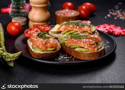 Open sandwich or toast. Grain bread with salmon, avocado and sesame seeds. Healthy snack, fat and omega 3 source on a christmas table. Toast sandwich with butter, avocado and salmon, decorated with arugula and sesame seeds, on a christmas table