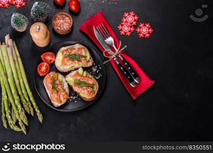 Open sandwich or toast. Grain bread with salmon, avocado and sesame seeds. Healthy snack, fat and omega 3 source on a christmas table. Toast sandwich with butter, avocado and salmon, decorated with arugula and sesame seeds, on a christmas table