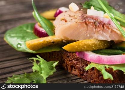 Open sandwich with young herring, herbs and pickled cucumber, close-up, selective focus. Traditional Danish smorrebrod. Sandwiches with matias herring arranged on a wooden background